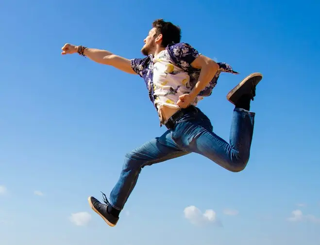 man in black shirt jumping on brown sand near body of water during daytime